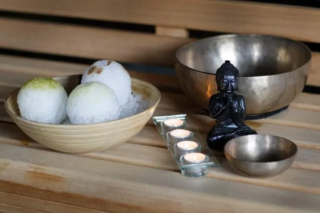 herzoklang, Badebomben, Handtücher, Glocken, Kerzen und ein kleines Buddha-Dekostück auf einem Tisch