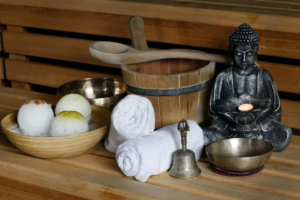 herzoklang, Badebomben, Handtücher, Glocken, Kerzen und ein kleines Buddha-Dekostück auf einem Tisch