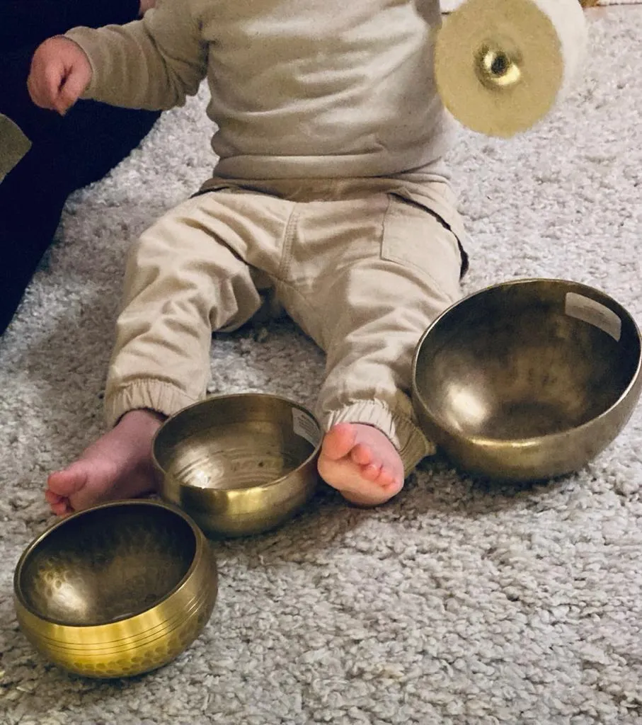 herzoklang, ein Baby, das zwischen heilenden Klangschalen sitzt und eine Klangscheibe in den Händen hält
